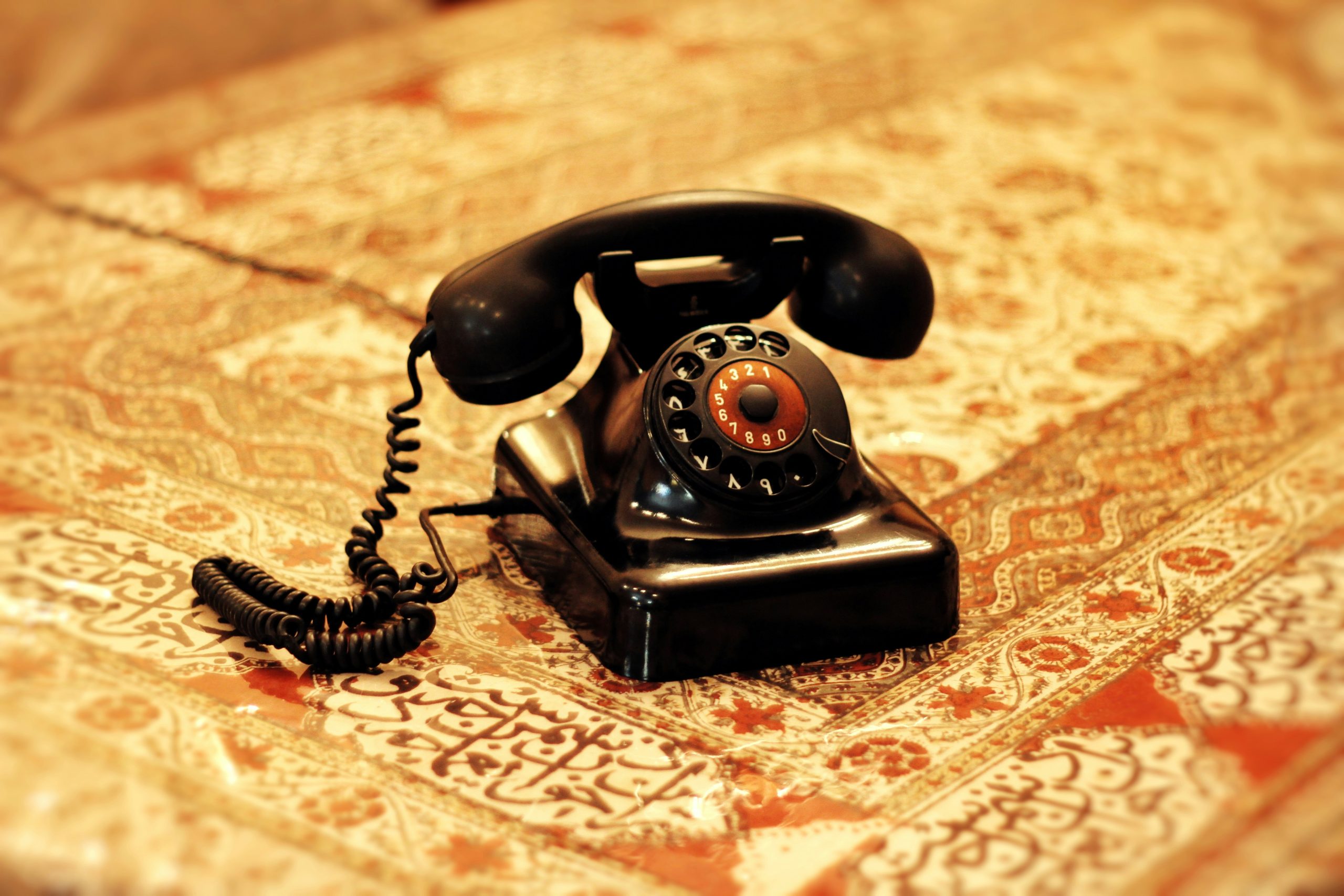 Antique black rotary dial telephone sitting on an ornate patterned tablecloth